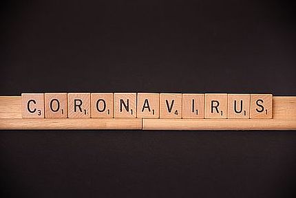 "Coronavirus" Holz- Scrabble Buchstaben aneinandergereiht, sodass Coronavirus zu lesen ist. Schwarzer Hintergrund. 