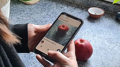 Eine Frau hält ihr Handy über einen Apfel, um mit der Bilderkennung ein Rezept zu finden.