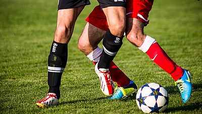 Foto als Zoom auf Beine beim Fußballspielern und einen Fußball, als Symbolik für Fußball