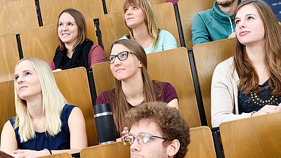 Sieben Studierende sitzen in einem Hörsaal.