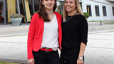 Zwei junge Frauen vor einem Gebäude.