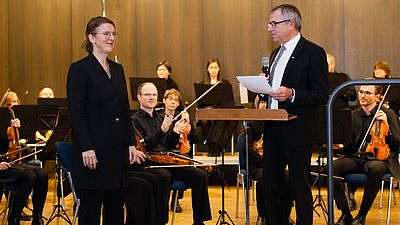 Mann und Frau stehen vor einem Orchester und reden