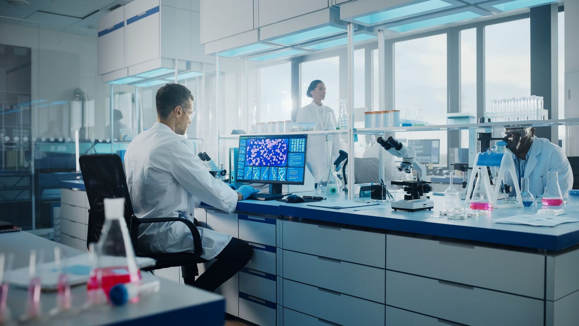 Medical Science Laboratory with Diverse Multi-Ethnic Team of Biotechnology Scientists Developing Drugs, Microbiologist Working on Computer with Display Showing Gene Editing Interface.