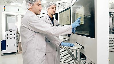 Zwei Männer stehen in weißen Reinraumanzügen in einem Labor und bedienen eine Maschine.