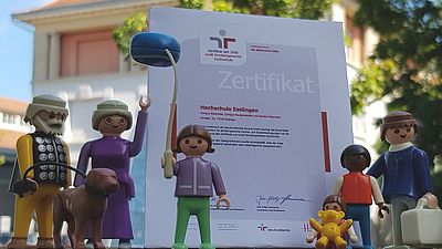 Eine Playmobil-Figuren Familie ist um ein Zertifikat herum angeordnet.