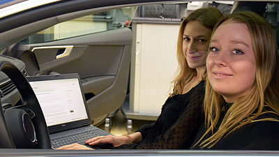 Zwei junge Frauen sitzen vorne in einem Auto.