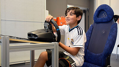 Ein Junge sitzt im Fahrsimulator und lenkt das virtuelle Auto über eine Rennstrecke.