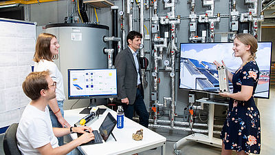 Drei Studierende und ein Professor stehen im Labor für Gebäude-, Energie- und Umwelttechnik.