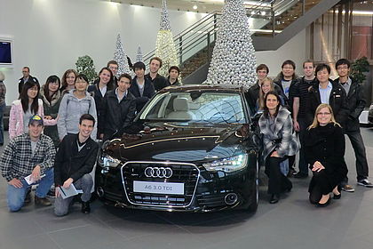  Group of students around a black Audi limousine, artificial silver fir trees in the background