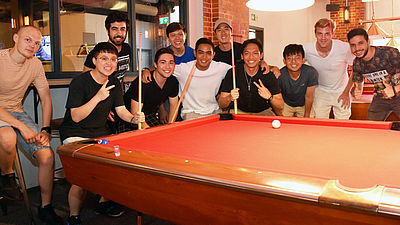 Eine Grupper junger Männer steht am Billiardtisch.
