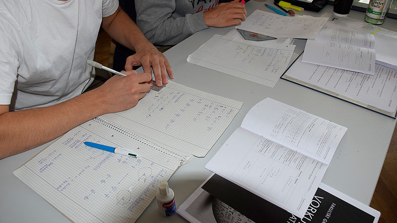 Studierende im Mathekurs berechnen Aufgaben und üben. Die Unterlagen liegen auf dem Tisch.å