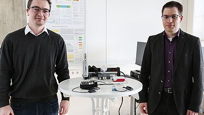 Professor und ein studentischer Mitarbeiter mit einem Versuchsaufbau in der IT