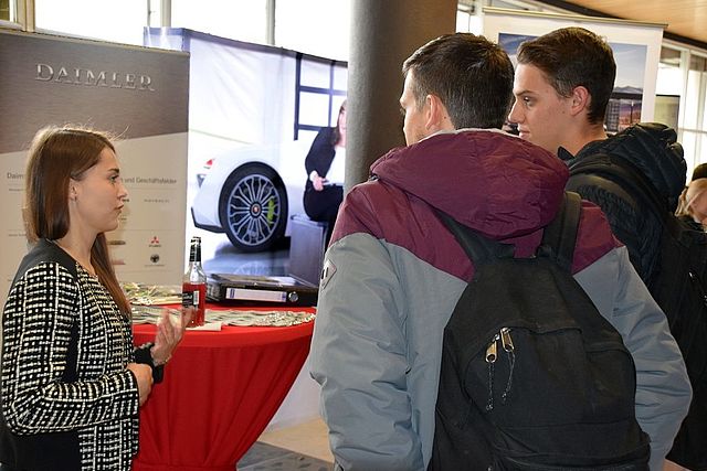 Daimler company representative in conversation with two students 