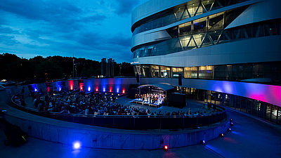 Das Mercedes-Benz-Museum mit der Open-Air Bühne vor einem Abendhimmel.