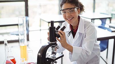 Mädchen mit Kittel und Schutzbrille am Mikroskop