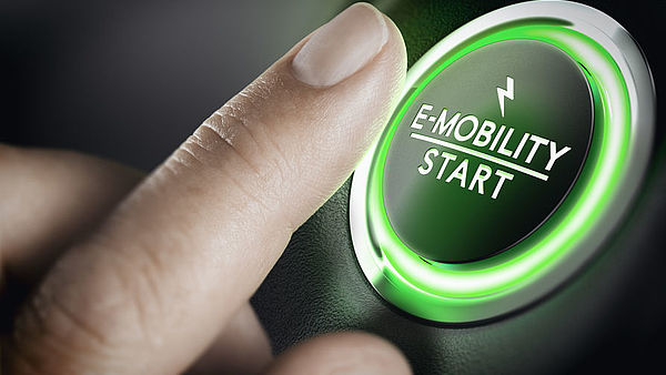 Finger drückt auf einen grünen Knopf mit Aufschrift E-Mobility
