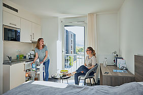 In einem Zimmer einer Wohnanlage des Studierendenwerks Stuttgart sitzen zwei Frauen und unterhalten sich.