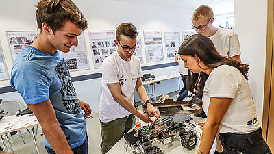 Vier Schüler der Schüler-Ingenieur-Akademie stehen um einen Tisch und  präsentieren ein ferngesteuertes Auto.
