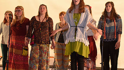 Solo-Sängerin in Hippie-Kleidung wird von Chor begleitet