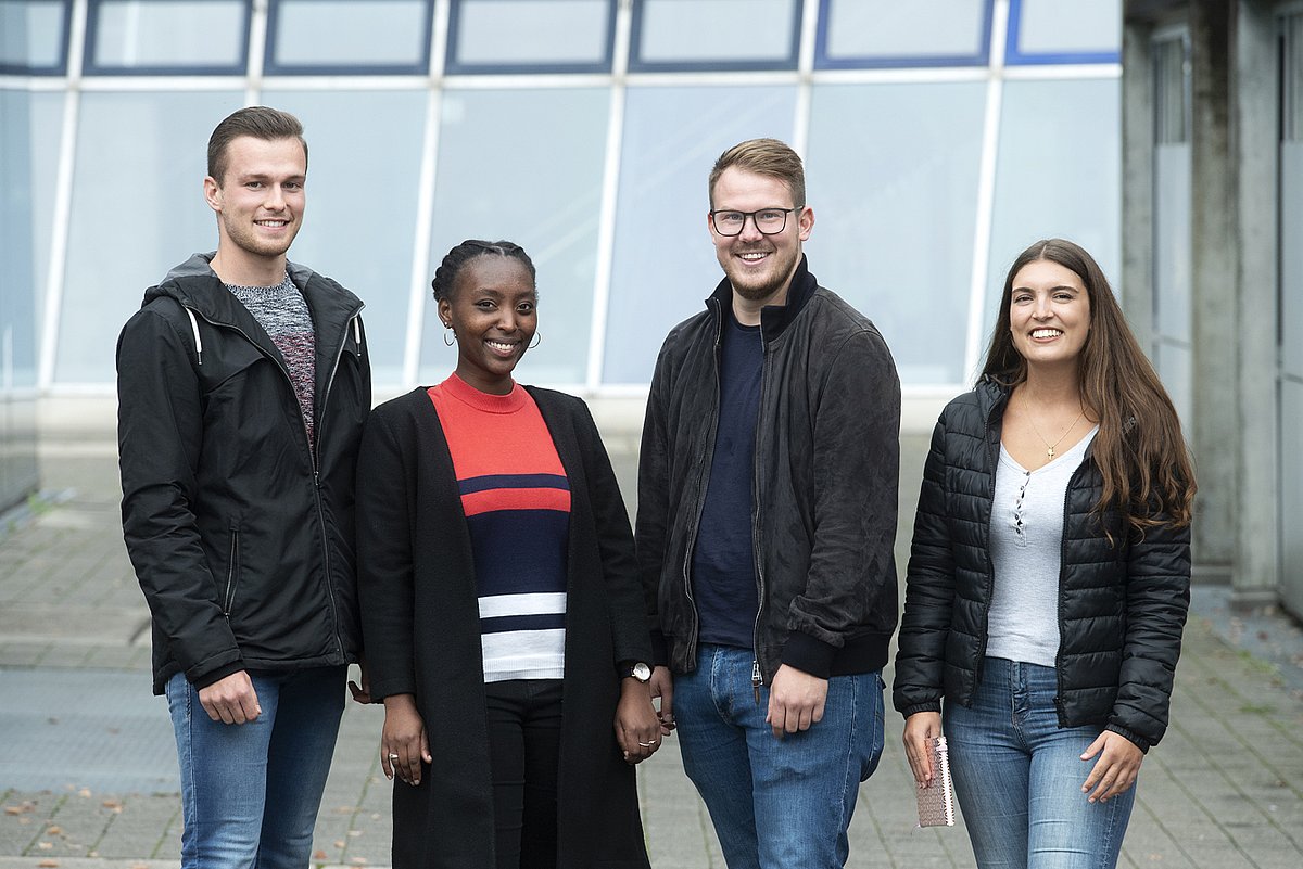 Zwei weibliche und zwei männliche Studierende stehen nebeneinander uf dem Campus Stadtmitte und lächeln in die Kamera 