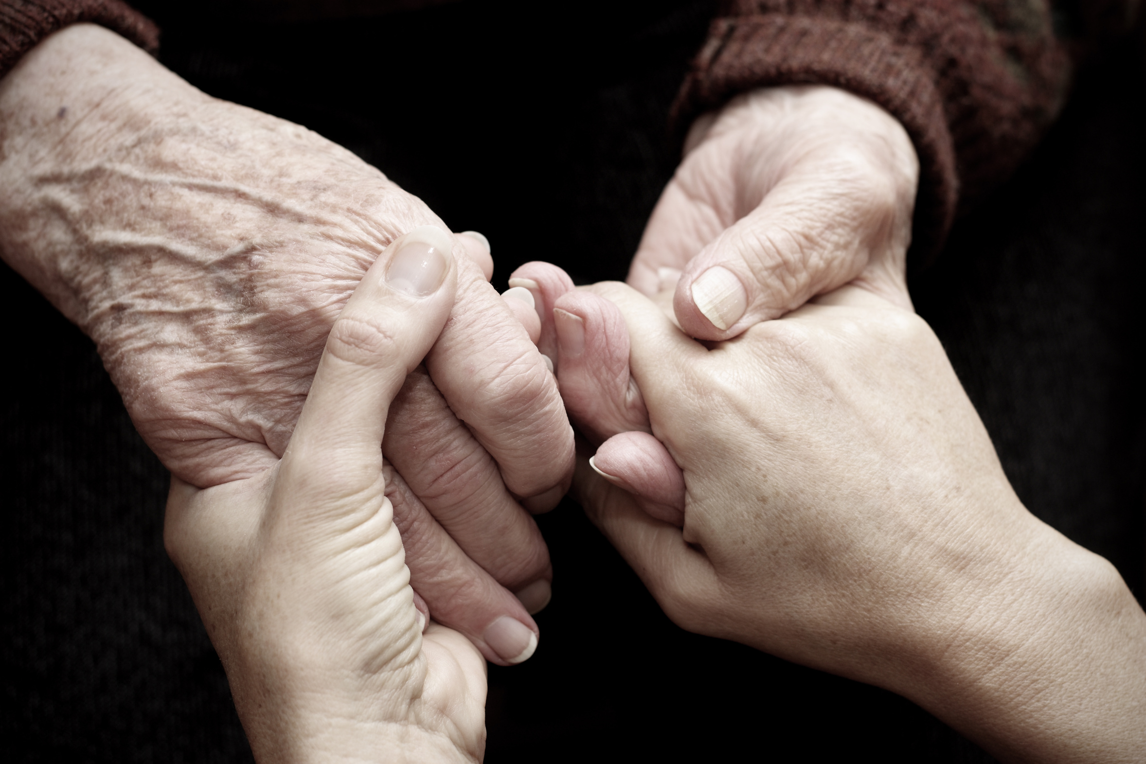 Nahaufnahme einer alten Person und einer jungen Person die Händchen halten 